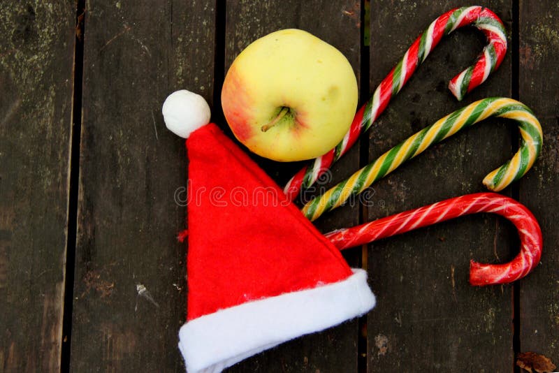 Una mela, cappello rosso di Babbo Natale, tre lollipope di caramella su fondo marrone scuro. fotografia stock libera da diritti Una mela, cappello rosso di Babbo Natale, tre lollipope di caramella su fondo marrone scuro. fotografia stock libera da diritti