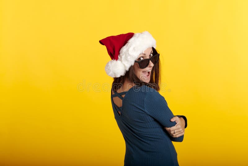 Una morena con un sombrero de santa claus con fondo amarillo y gafas de sol foto de archivo