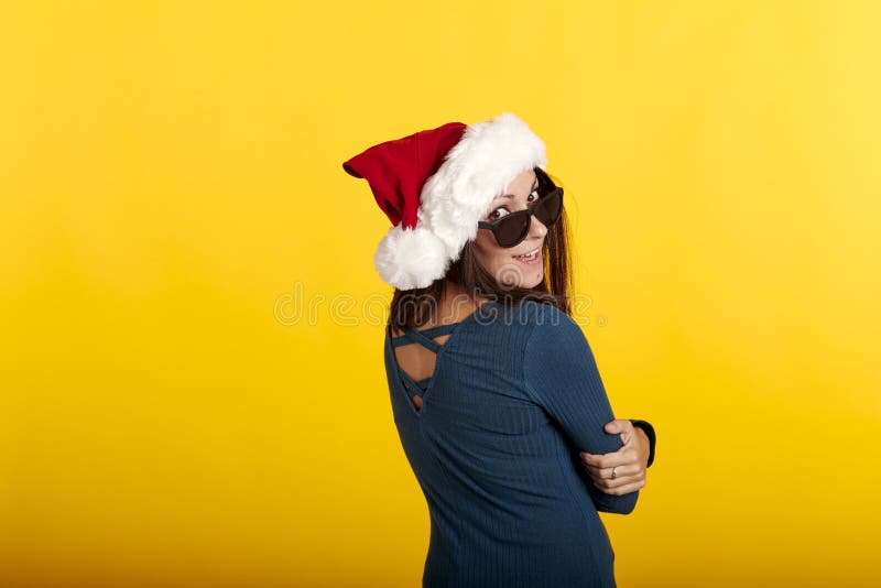 Una morena con un sombrero de santa claus con fondo amarillo y gafas de sol fotos de archivo libres de regalías