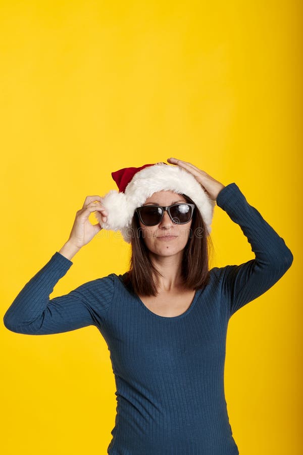 Una morena con un sombrero de santa claus con fondo amarillo y gafas de sol imagenes de archivo