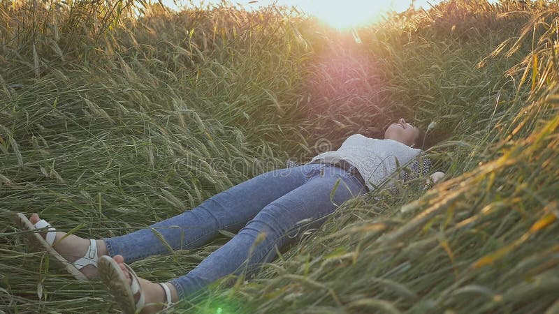 Una muchacha adolescente hermosa joven cae en un campo de trigo en una puesta del sol suave