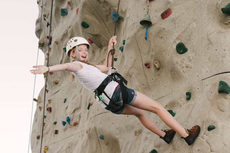 Una muchacha adolescente que sube en una pared de la roca que se inclina detrás contra el dispositivo de protección en caso de vol