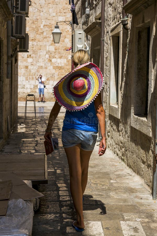 Una muchacha con un sombrero hermoso grande está caminando a lo largo de la calle de la ciudad vieja fotos de archivo libres de regalías Una muchacha con un sombrero hermoso grande está caminando a lo largo de la calle de la ciudad vieja fotos de archivo libres de regalías