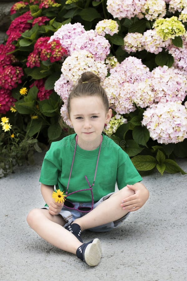 Una muchacha de cuatro años delante de varias plantas florecientes foto de archivo Una muchacha de cuatro años delante de varias plantas florecientes foto de archivo