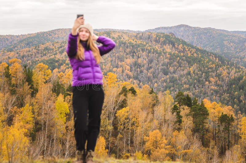 Una muchacha en una chaqueta de la lila hace un salfi en una montaña, una visión de las montañas y un bosque otoñal por un día nu fotos de archivo libres de regalías Una muchacha en una chaqueta de la lila hace un salfi en una montaña, una visión de las montañas y un bosque otoñal por un día nu fotos de archivo libres de regalías