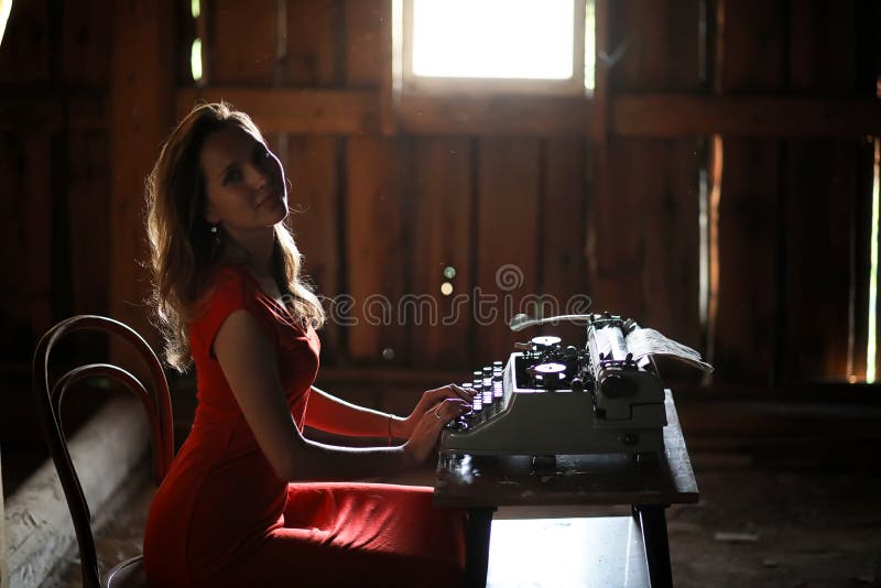 Una muchacha en estilo retro imprime en una máquina de escribir vieja. Silueta de una muchacha hermosa en un vestido rojo en el fondo de una ventana en un viejo houser