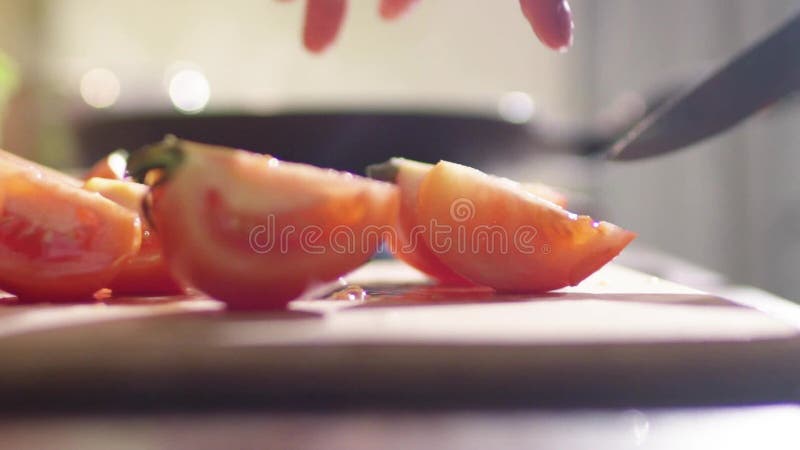 Una muchacha está cocinando una ensalada en la cocina Ella corta el tomate jugoso rojo en muchos pequeños pedazos almacen de metraje de vídeo