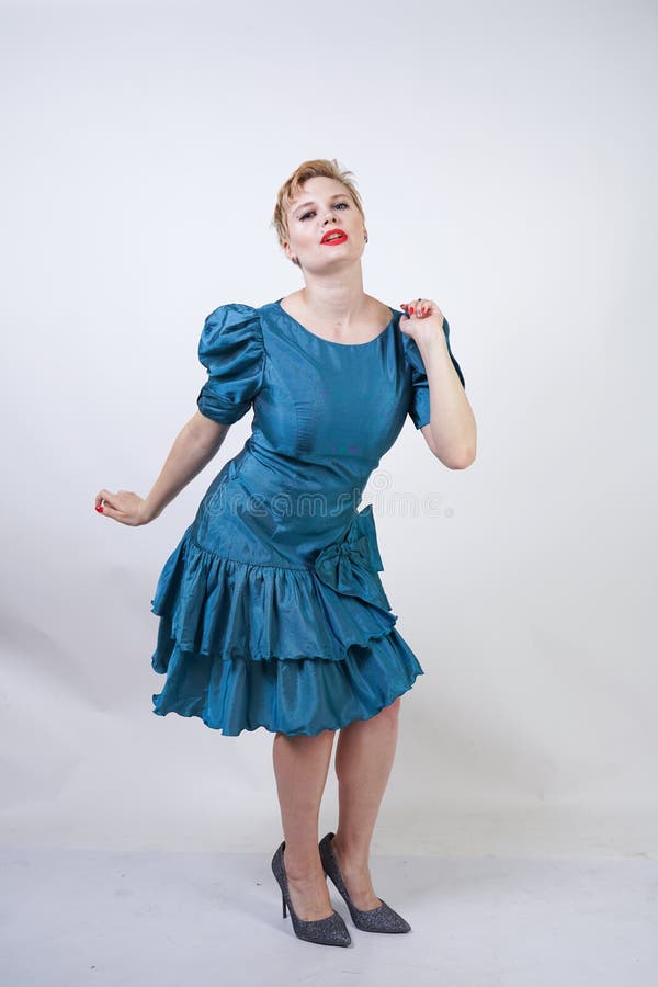 Una muchacha hermosa con una figura del tamaño extra grande vestida en un vestido retro lindo y soportes de la moda en un fondo b foto de archivo Una muchacha hermosa con una figura del tamaño extra grande vestida en un vestido retro lindo y soportes de la moda en un fondo b foto de archivo