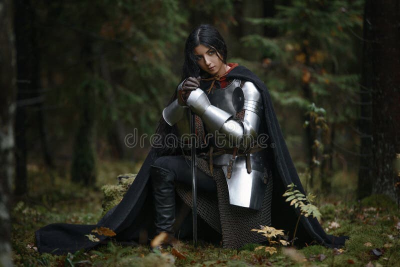 Una muchacha hermosa del guerrero con un chainmail que lleva de la espada y armadura en un bosque misterioso foto de archivo libre de regalías Una muchacha hermosa del guerrero con un chainmail que lleva de la espada y armadura en un bosque misterioso foto de archivo libre de regalías