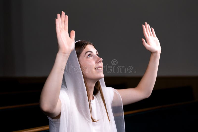 Una muchacha modesta joven con un pañuelo en su cabeza se está sentando en iglesia y está rogando El concepto de religión, rezo
