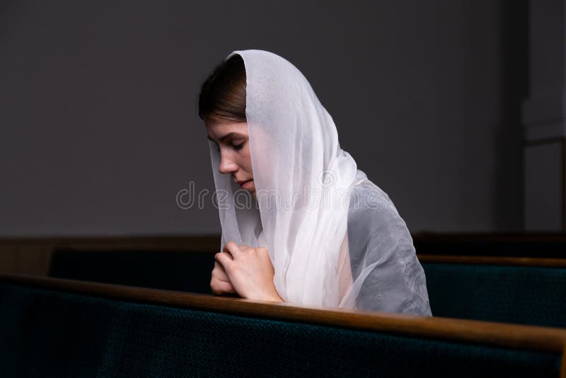 Una muchacha modesta joven con un pañuelo en su cabeza se está sentando en iglesia y está rogando El concepto de religión, rezo