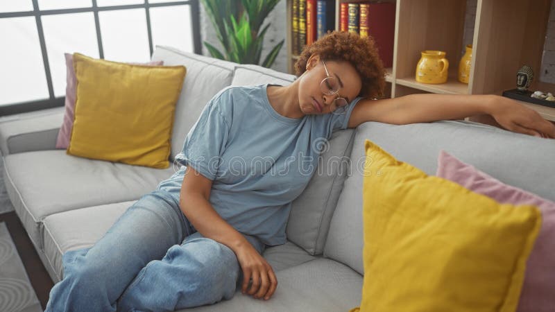Una mujer afroamericana descansa sobre un sofá en una acogedora sala de estar que encarna la paz y la relajación en casa fotos de archivo libres de regalías