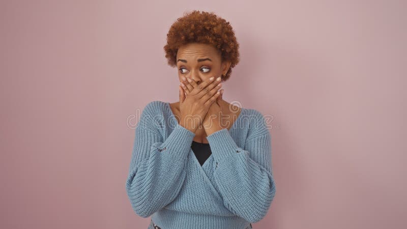 Una mujer afroamericana sorprendida con la boca sobre el fondo rosado foto de archivo