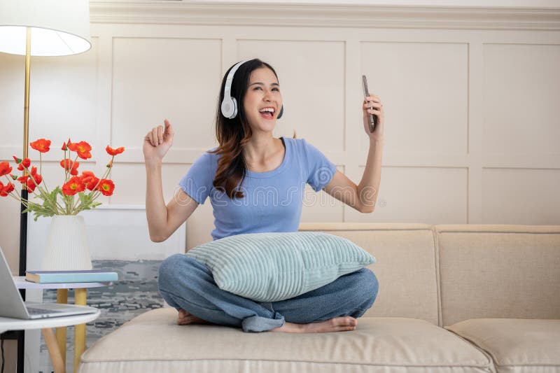 Una mujer asiática alegre escuchando la música y bailando la canción en su salón fotografía de archivo libre de regalías