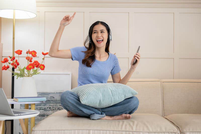 Una mujer asiática alegre escuchando la música y bailando la canción en su salón imágenes de archivo libres de regalías