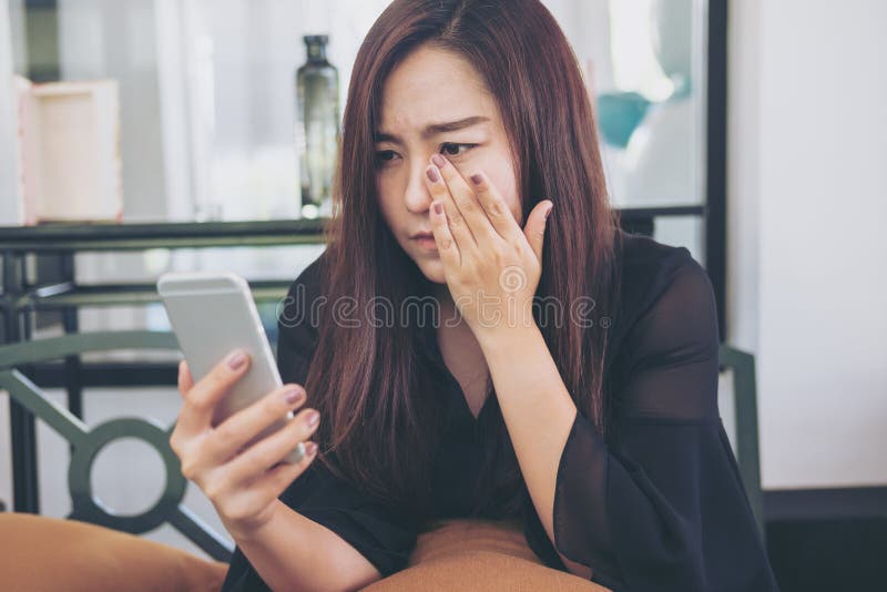 Una mujer asiática hermosa que mira el teléfono elegante con la sensación triste y el grito fotografía de archivo Una mujer asiática hermosa que mira el teléfono elegante con la sensación triste y el grito fotografía de archivo