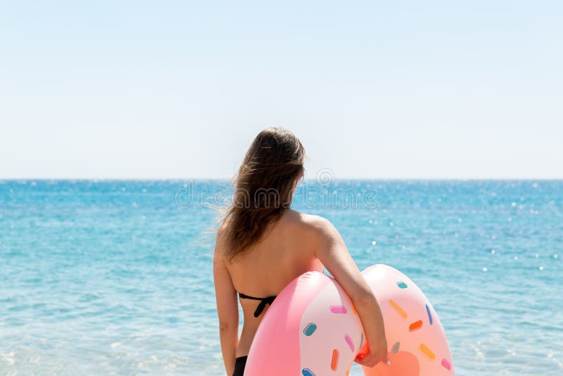 Una mujer camina en la agua de mar Muchacha que se relaja en el anillo inflable en la playa Vacaciones de verano y concepto de la foto de archivo Una mujer camina en la agua de mar Muchacha que se relaja en el anillo inflable en la playa Vacaciones de verano y concepto de la foto de archivo