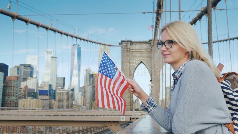 Una mujer con la bandera de América en sus soportes de la mano en el puente de Brooklyn con vistas a Manhattan Turismo en los E.E imágenes de archivo libres de regalías Una mujer con la bandera de América en sus soportes de la mano en el puente de Brooklyn con vistas a Manhattan Turismo en los E.E imágenes de archivo libres de regalías