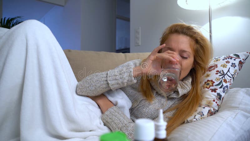 Una mujer con la fiebre que miente en el sofá con un termómetro en su boca carro almacen de metraje de vídeo