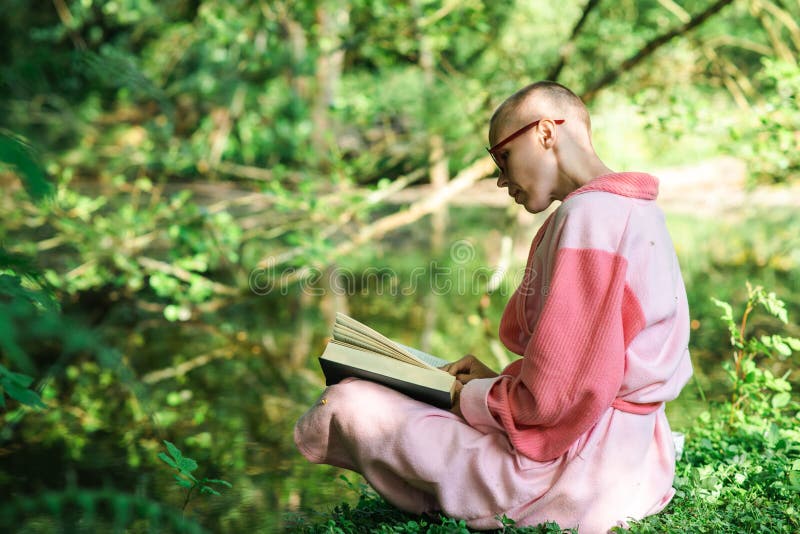 A woman with a short haircut reads a book on the shore of the lake against the backdrop of green nature. Sunny day. A woman in a bathrobe. A woman with a short haircut reads a book on the shore of the lake against the backdrop of green nature. Sunny day. A woman in a bathrobe.