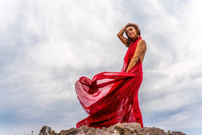 Una Mujer Con Un Vestido Rojo Se Alza Sobre Un Cielo Tormentoso Con Su Vestido Revoloteando El Tejido Volando En El Viento. de archivo Imagen de retroceder, 234961874
