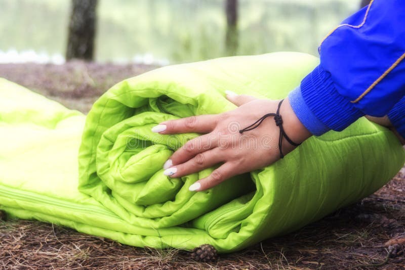 Una mujer dobla y embala un saco de dormir, pasando en un viaje a través del bosque el concepto de turismo y de turismo ecológico foto de archivo libre de regalías Una mujer dobla y embala un saco de dormir, pasando en un viaje a través del bosque el concepto de turismo y de turismo ecológico foto de archivo libre de regalías