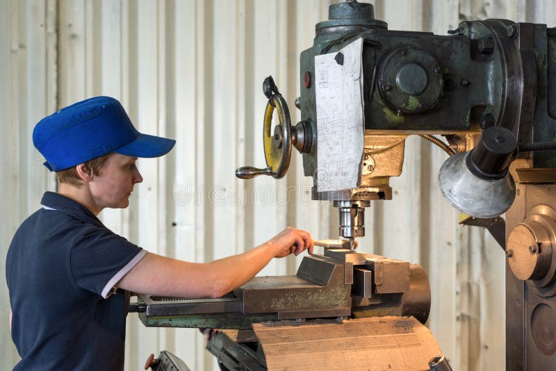 Una mujer en el trabajo sobre una fresadora vertical El trabajar a máquina de una pieza de metal en una máquina para corte de met imagen de archivo libre de regalías Una mujer en el trabajo sobre una fresadora vertical El trabajar a máquina de una pieza de metal en una máquina para corte de met imagen de archivo libre de regalías