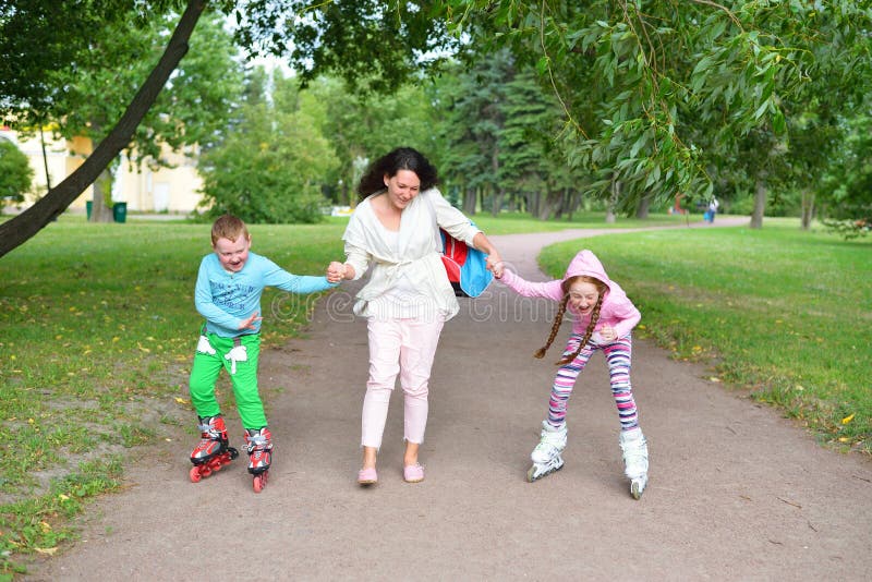 Una mujer enseña a los niños riéndose a patinar sobre ruedas en el parque fotos de archivo