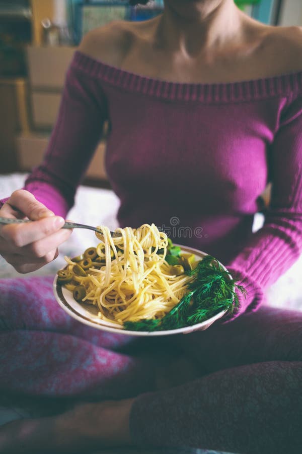 Una mujer está comiendo las pastas con las hierbas Desayuno en cama La muchacha está envolviendo los espaguetis en la bifurcación Comida vegetariana Comida hecha en casa
