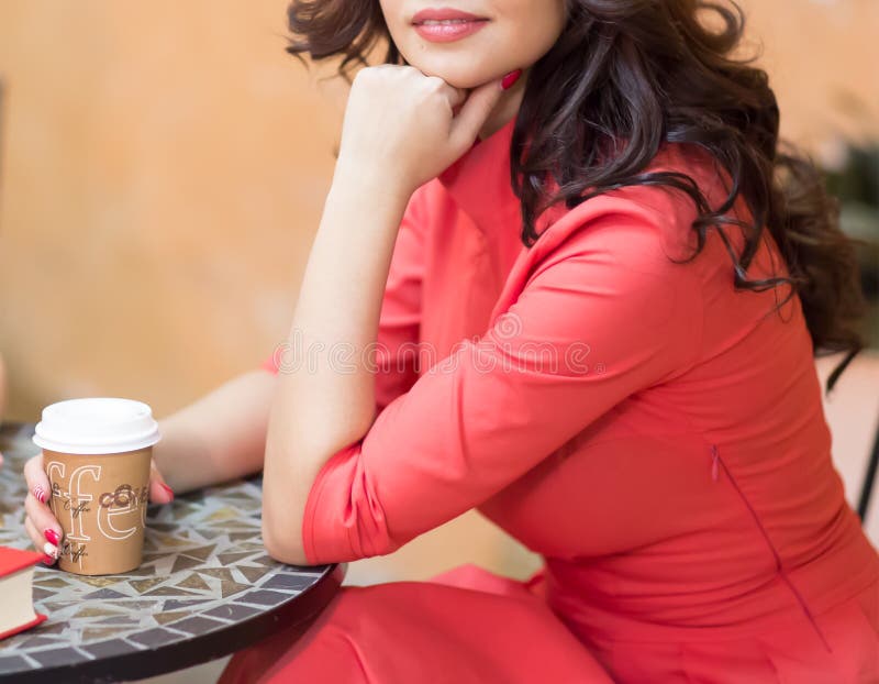 Una mujer está sosteniendo una cartulina de cristal con el café, sentándose en una tabla en un café acogedor foto de archivo Una mujer está sosteniendo una cartulina de cristal con el café, sentándose en una tabla en un café acogedor foto de archivo