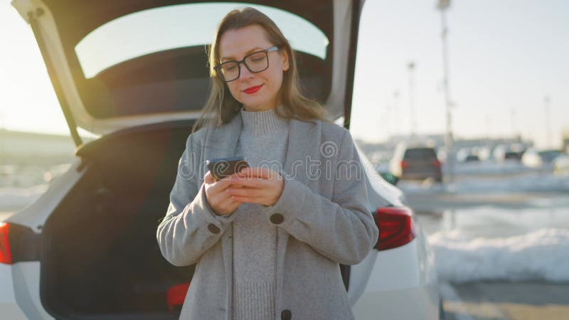 Una mujer está usando su smartphone mientras está de pie junto a un coche durante la temporada de invierno metrajes
