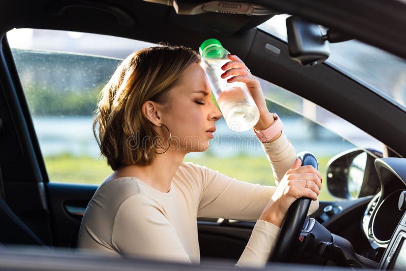 Una mujer exhausta que conduce siente dolor de cabeza sentada dentro de su auto aplica una botella de agua a su frente clima calur