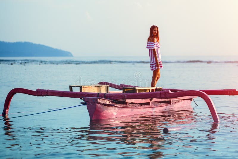 Una mujer joven con una sonrisa acompaña la situación de la puesta del sol en un bote pequeño rosado imágenes de archivo libres de regalías Una mujer joven con una sonrisa acompaña la situación de la puesta del sol en un bote pequeño rosado imágenes de archivo libres de regalías