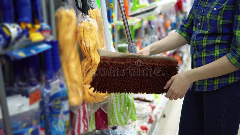 Una mujer joven elige una fregona en el supermercado