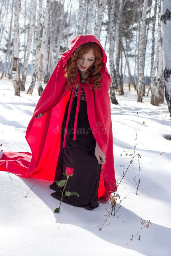 Una mujer joven en un impermeable rojo encontró una rosa en la nieve imagen de archivo Una mujer joven en un impermeable rojo encontró una rosa en la nieve imagen de archivo