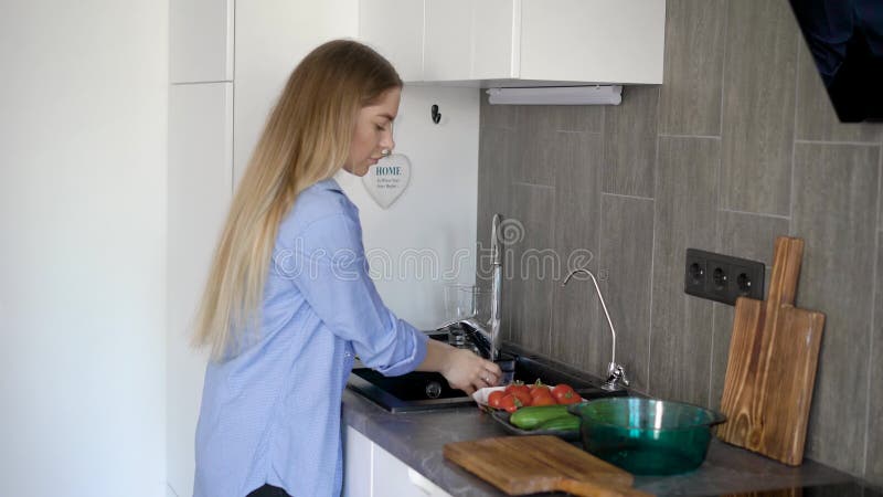 Una mujer joven lava verduras frescas para hacer una ensalada ligera de los tomates y de los pepinos, que ella cortará