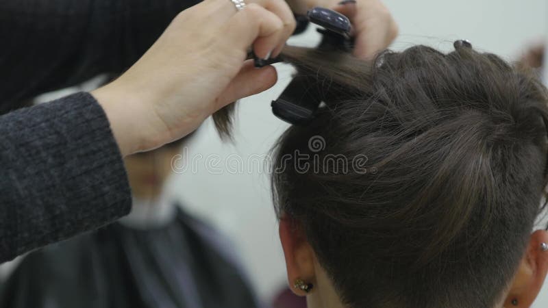 Una mujer joven se sienta en una butaca del ` s del peluquero: un peluquero hace diseñar del pelo Una mujer de pelo rubio joven v