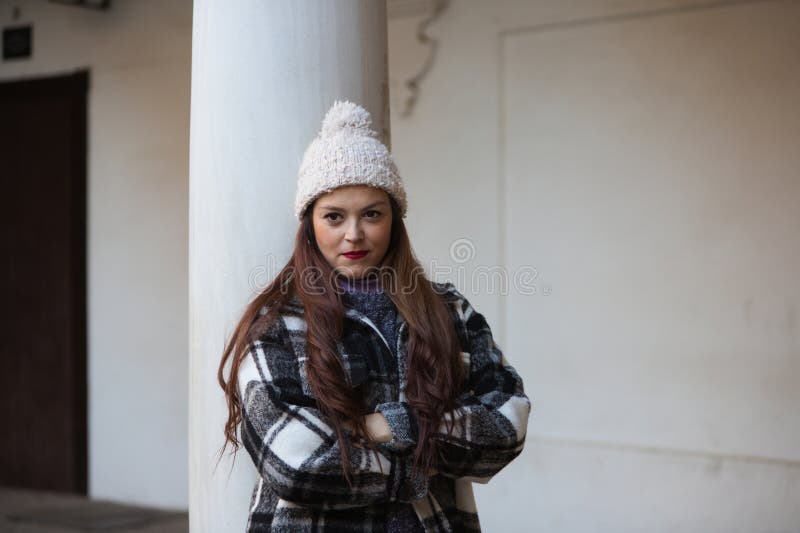 Una Mujer Joven Y Hermosa De Pelo Largo Marrón, Un Abrigo De De Lana Y Un Sombrero De Lana Se Inclina En Una Columna M Foto archivo - Imagen