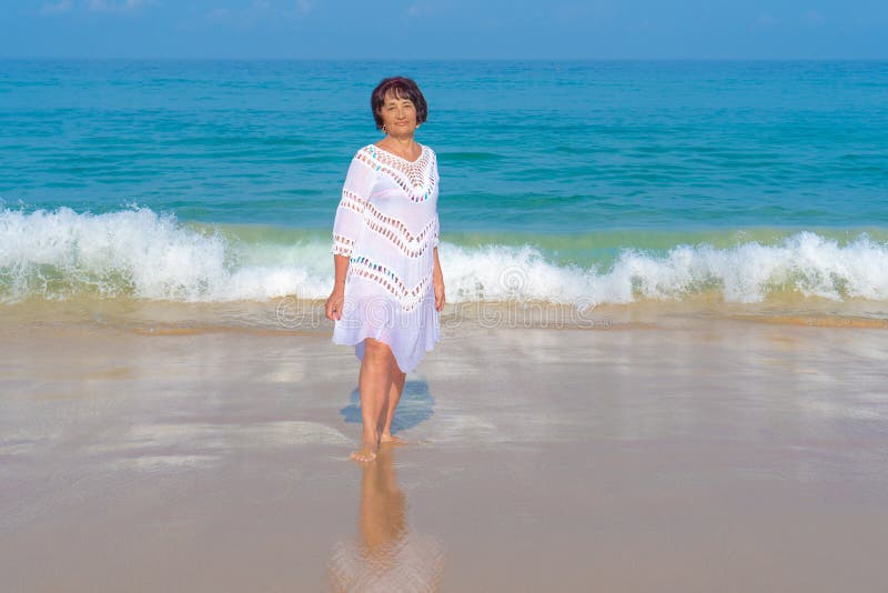 Una mujer mayor con el pelo negro en el soporte blanco del vestido contra el mar Personas mayores fotografía de archivo libre de regalías Una mujer mayor con el pelo negro en el soporte blanco del vestido contra el mar Personas mayores fotografía de archivo libre de regalías
