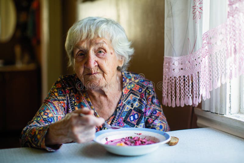 Una mujer mayor que come la sopa que se sienta en una tabla imagenes de archivo