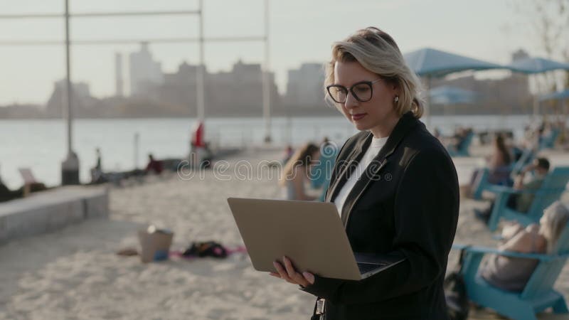 Una mujer profesional está trabajando activamente en su laptop mientras disfruta de la vista de la playa metrajes