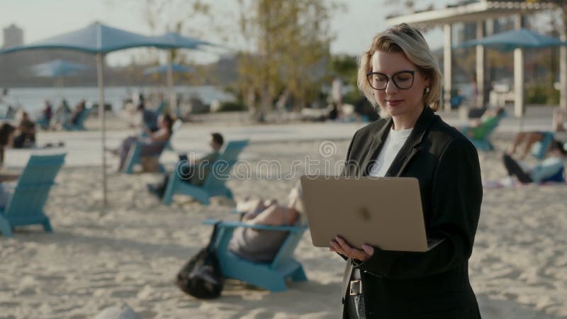 Una mujer profesional está trabajando activamente en su laptop mientras disfruta de la vista de la playa metrajes