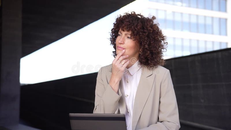 Una mujer profesional está trabajando activamente en una tableta mientras se encuentra en un entorno urbano cercano almacen de metraje de vídeo