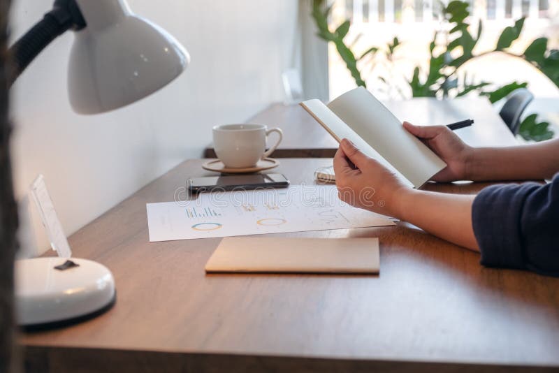 Una mujer que sostiene y que abre un cuaderno en blanco con la taza y los papeles de café en la tabla fotos de archivo Una mujer que sostiene y que abre un cuaderno en blanco con la taza y los papeles de café en la tabla fotos de archivo