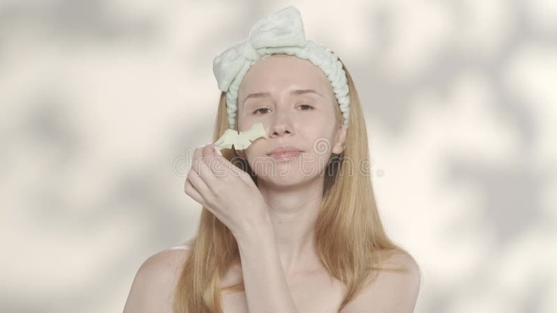 Una mujer realiza procedimientos cosméticos en un fondo gris con resplandor. una mujer con una banda para el pelo en la cabeza eli almacen de metraje de vídeo