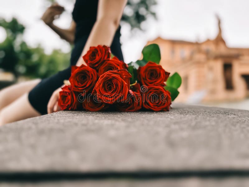 Una mujer sentada en un banco con un ramo de rosas rojas en el regazo fotografía de archivo