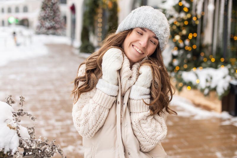 Una mujer sonriente con los ojos cerrados en un sombrero y mitones. hay nieve en el sombrero imagen de archivo libre de regalías
