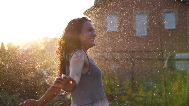Una mujer sonriente feliz está bajo la lluvia. impresionantes rayos solares dorados brillan en una joven lúdica disfrutando de una almacen de video