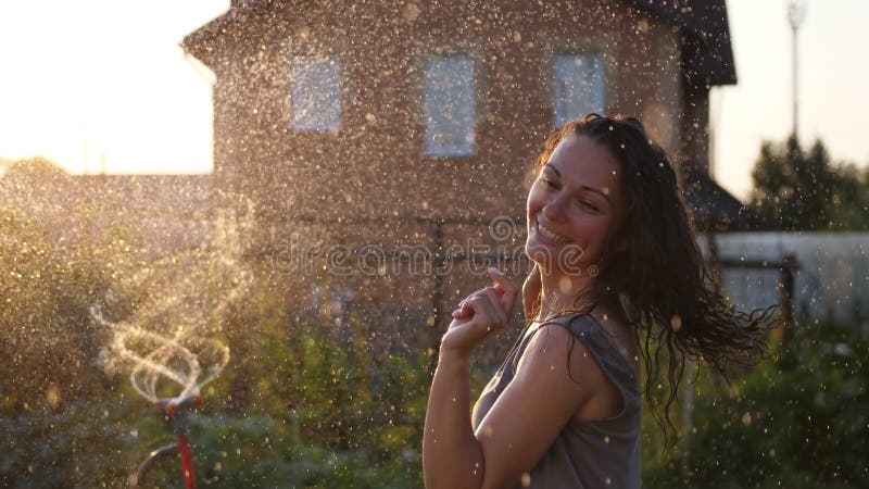 Una mujer sonriente feliz está bajo la lluvia. impresionantes rayos solares dorados brillan en una joven lúdica disfrutando de una metrajes