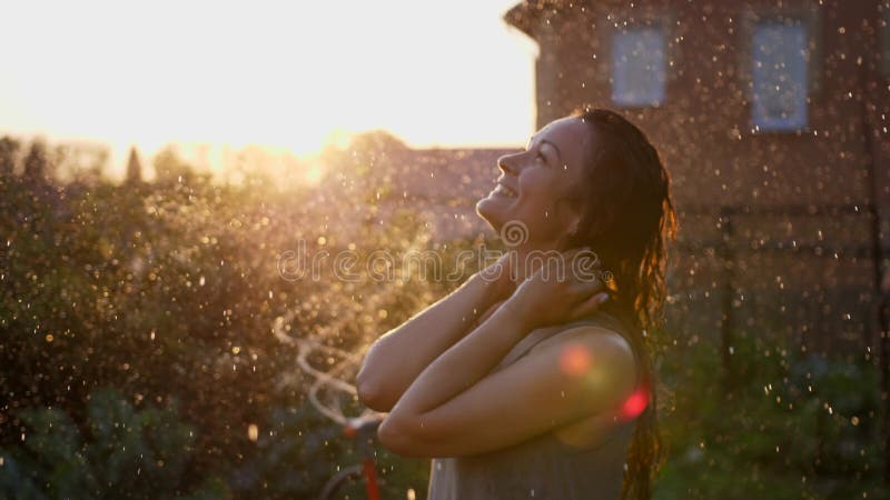 Una mujer sonriente feliz está bajo la lluvia. impresionantes rayos solares dorados brillan en una joven lúdica disfrutando de una almacen de video